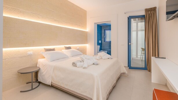 A modern hotel room with a large bed, bedside table, and a desk.