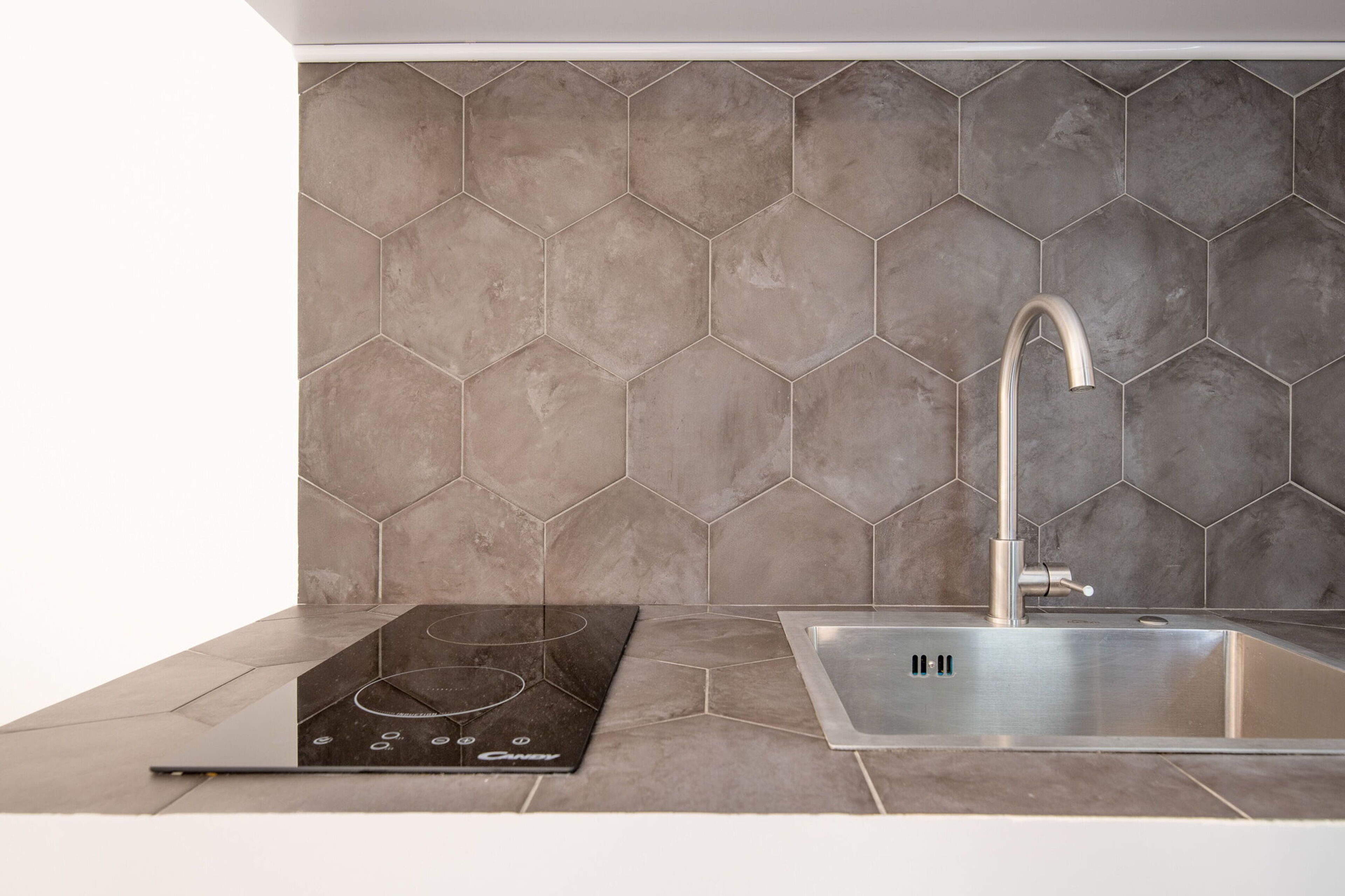 A kitchen with a hexagonal tile backsplash, a stainless steel sink, and a black induction cooktop.