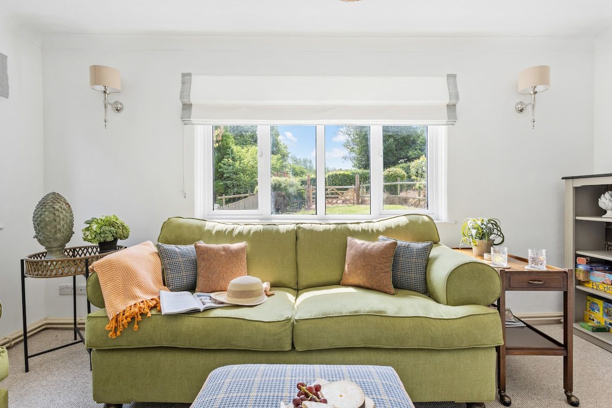 A room with a green sofa, a small table with a plant, and a window with a view of greenery.