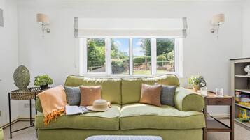 A room with a green sofa, a small table with a plant, and a window with a view of greenery.