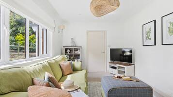 A living room with a sofa, ottoman, television, and artwork on the wall.