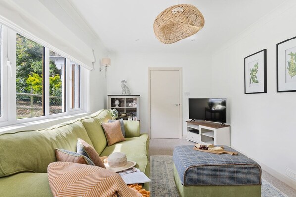 A living room with a sofa, ottoman, television, and artwork on the wall.