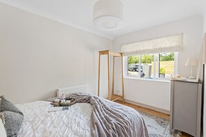 A bedroom with a bed, a window with a view, a radiator, and a bedside table.