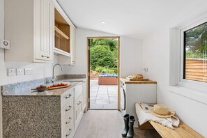 A compact kitchen with granite countertops, a built-in oven, and a view of a garden and hot tub outside. - Bramblewood (Maidencombe)