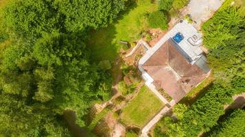 An aerial view of a property with a large garden, a swimming pool, and a building with a sloped roof.