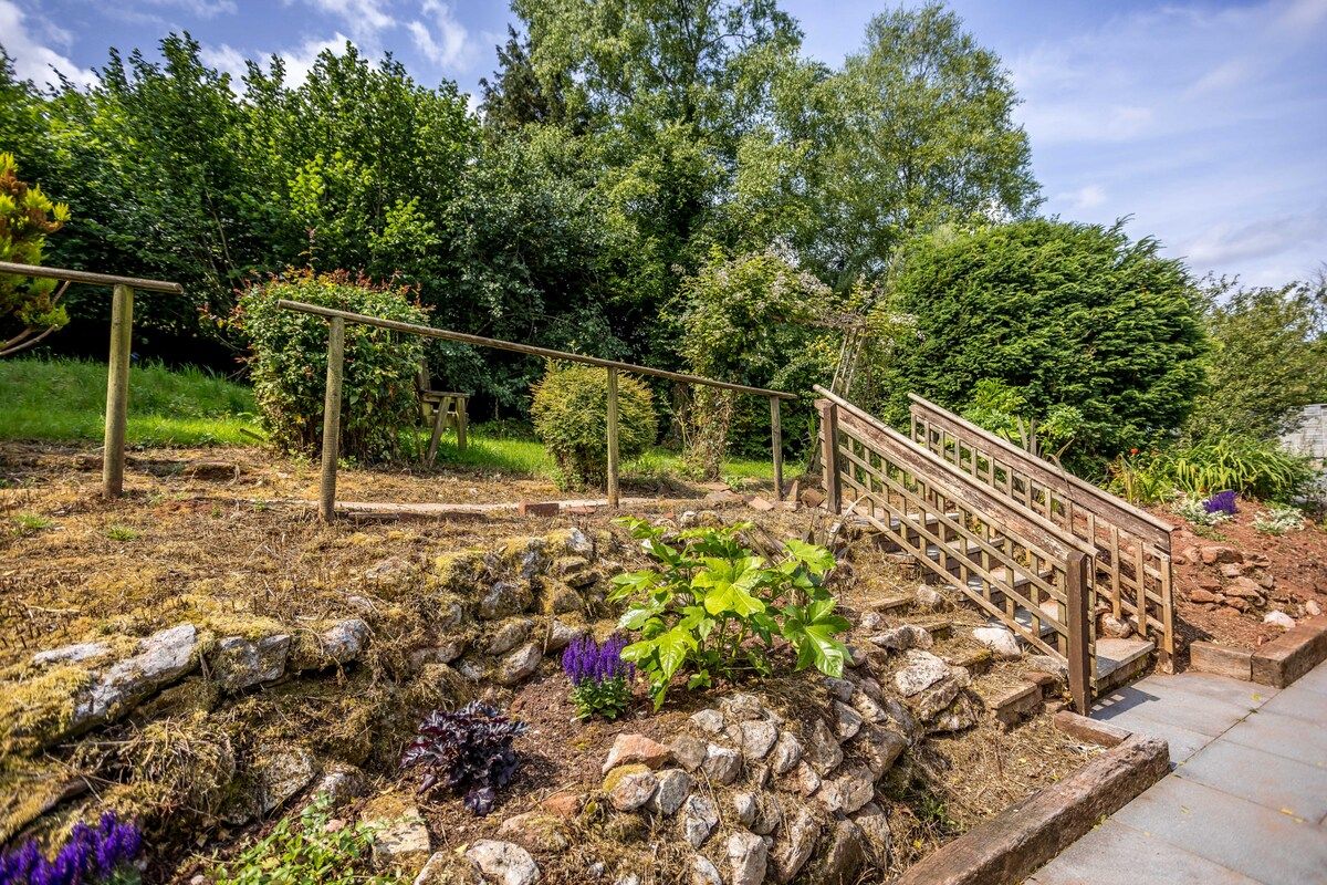 Un jardin agrémenté d’un escalier en bois, de murs en pierre et de diverses plantes.