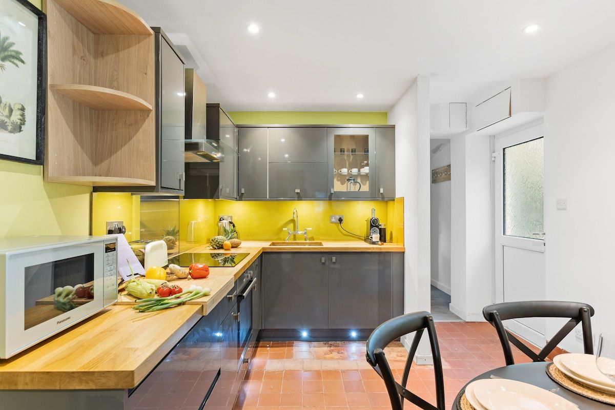 A modern kitchen with a microwave, wooden shelves, a sink, and a dining area with chairs.