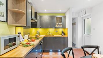 A modern kitchen with a microwave, wooden shelves, a sink, and a dining area with chairs.