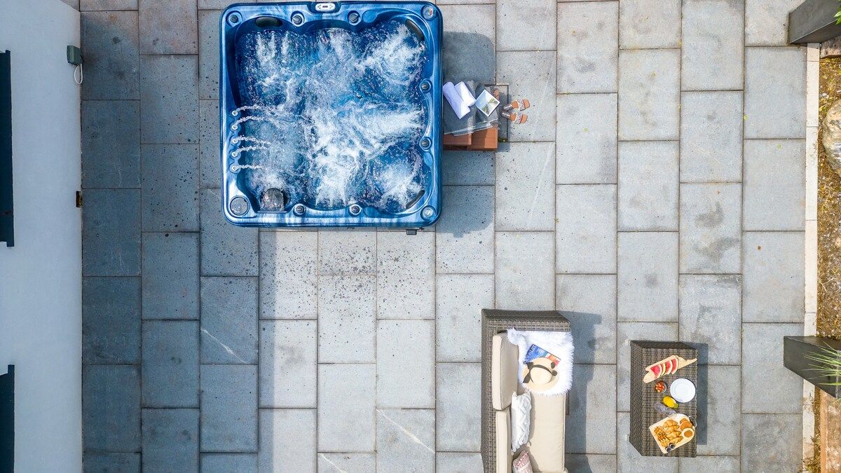 A hot tub on a paved patio with a towel and snacks nearby.