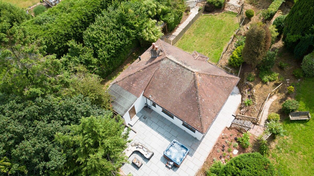 Une maison avec un toit en tuiles, un patio avec un jacuzzi et un jardin.