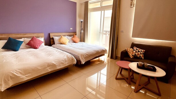Habitación de hotel con dos camas, un sofá, una mesita y una ventana con cortinas.