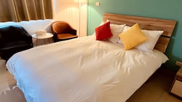 A hotel room with a large bed, a wooden headboard, a nightstand, a lamp, a chair, and a small table.