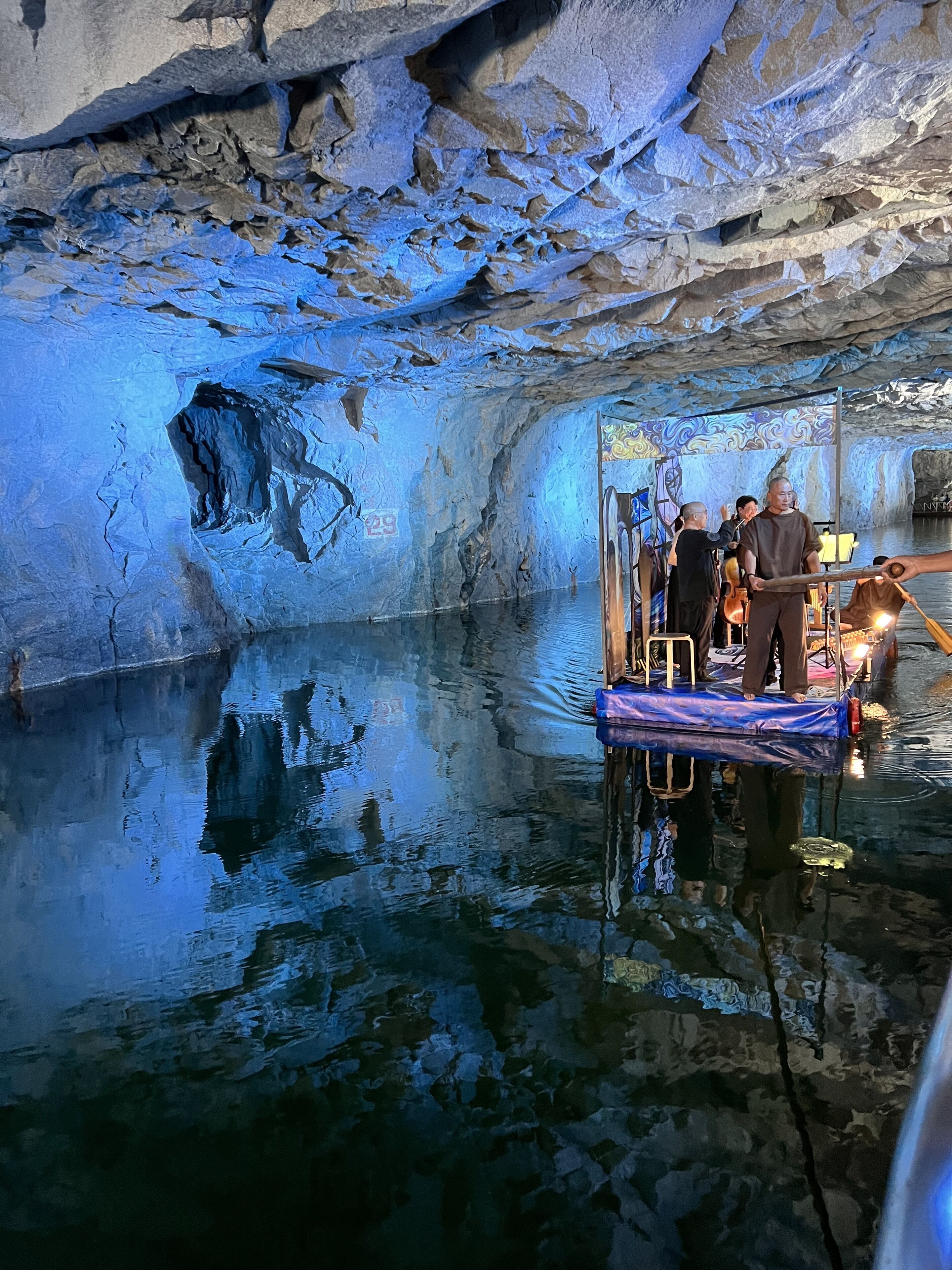 A cave interior with a reflective water surface, a wooden platform, and a person standing on it.
