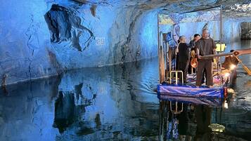 A cave interior with a reflective water surface, a wooden platform, and a person standing on it.