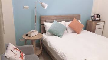 Habitación de hotel ordenada con cama, mesita de noche, lámpara, silla y una pequeña mesa con caja de pañuelos.