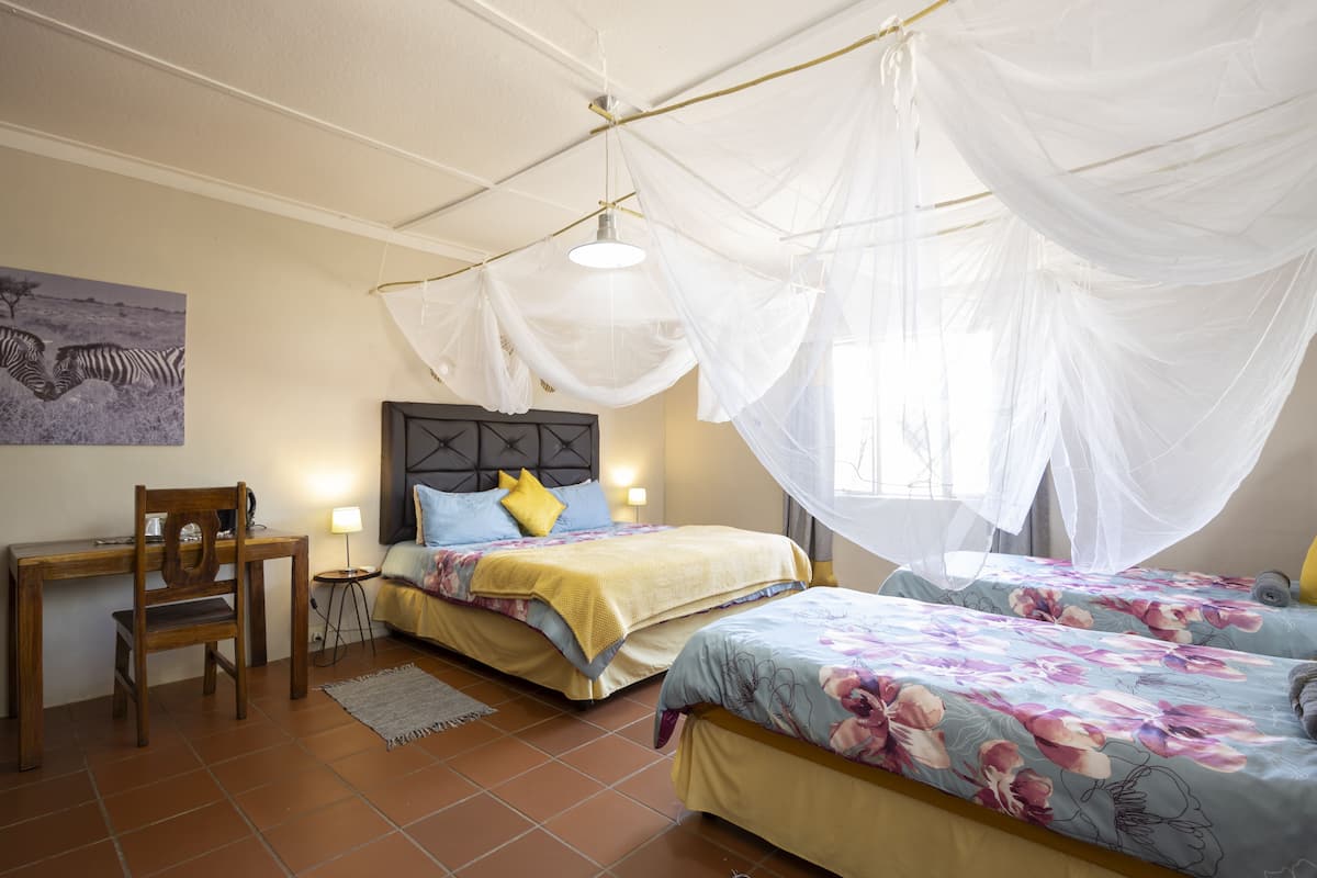 A bedroom with two beds, a wooden desk, a chair, and a nightstand with a lamp.