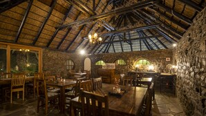 Un comedor rústico con mesas y sillas de madera, paredes de piedra y techo de paja.