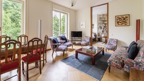 A spacious living room with a wooden dining table, floral armchairs, a sofa, and a television. - Milano Classy Heritage Home: quiet and prestigious apartment CITY CENTER - 4 BDR (Milano)