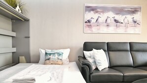 A modern bedroom with a bed, a black leather sofa, and a wall-mounted painting of seagulls. - Wohnung Wesernest in Büsum (Büsum)