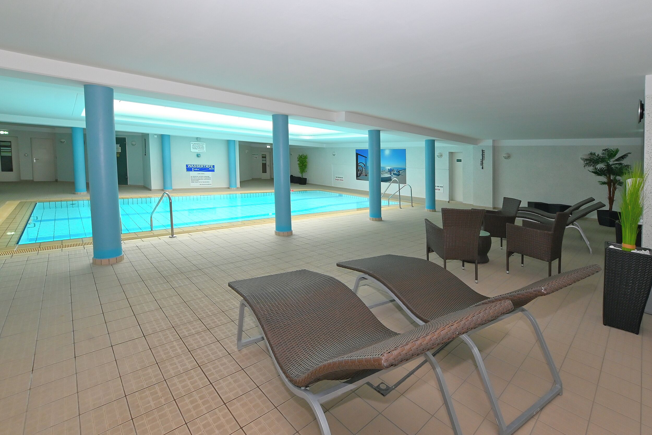Área interna de piscina com espreguiçadeiras e placa indicando zona de segurança aquática.