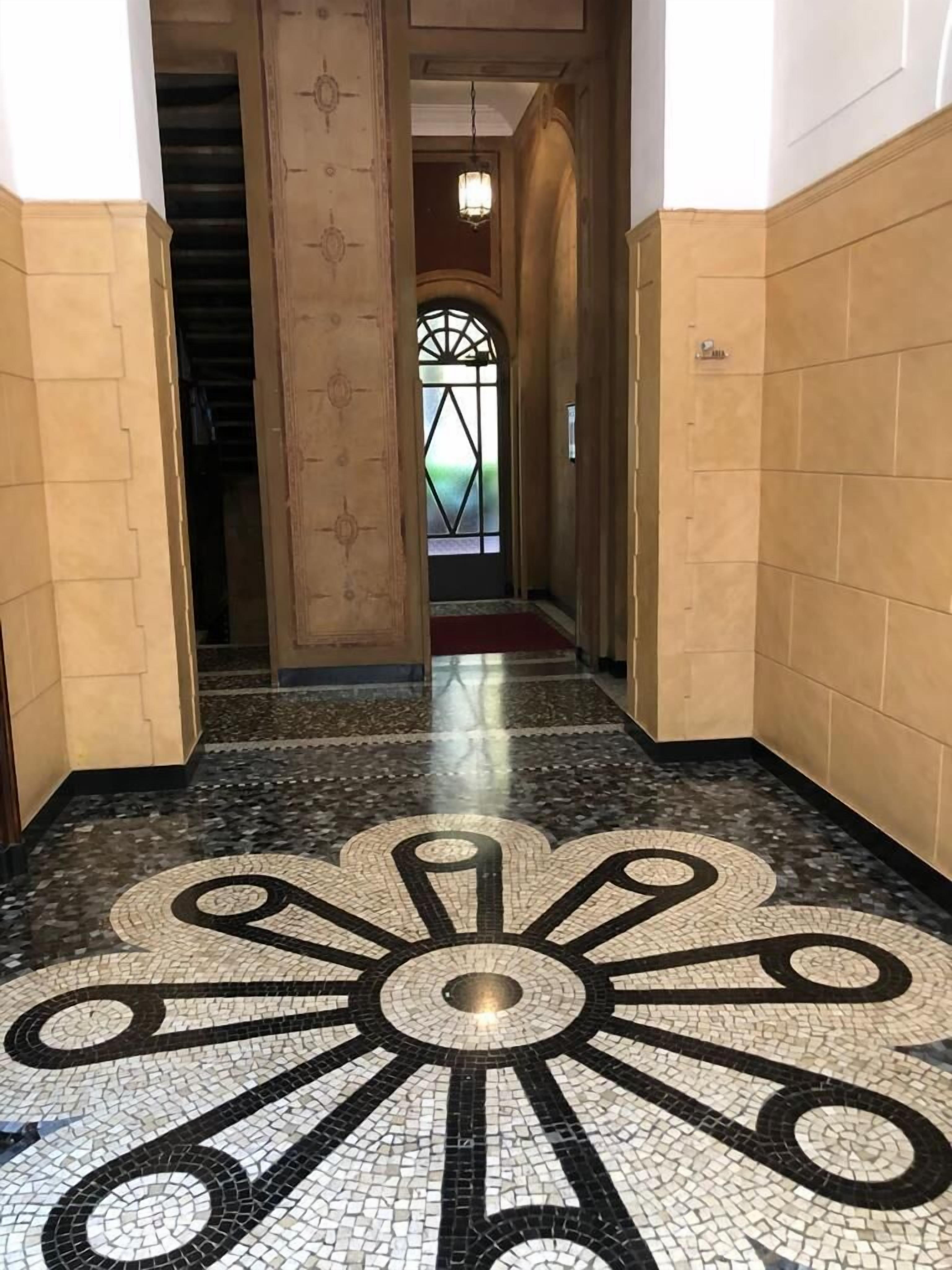 A hallway with a patterned floor, a staircase, and a door leading to a room.