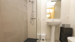 Une salle de bain moderne avec une douche à parois de verre, un lavabo sur colonne, des toilettes et un petit meuble de rangement.