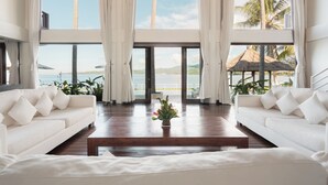 A spacious room with a large window overlooking a beach and ocean, featuring two white sofas and a wooden coffee table. - Villa Blanca by Alfred in Bali (Manggis)