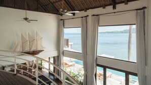 A spacious room with a large window overlooking a pool and the sea, a ceiling fan, and a hanging sailboat model. - Villa Blanca by Alfred in Bali (Manggis)