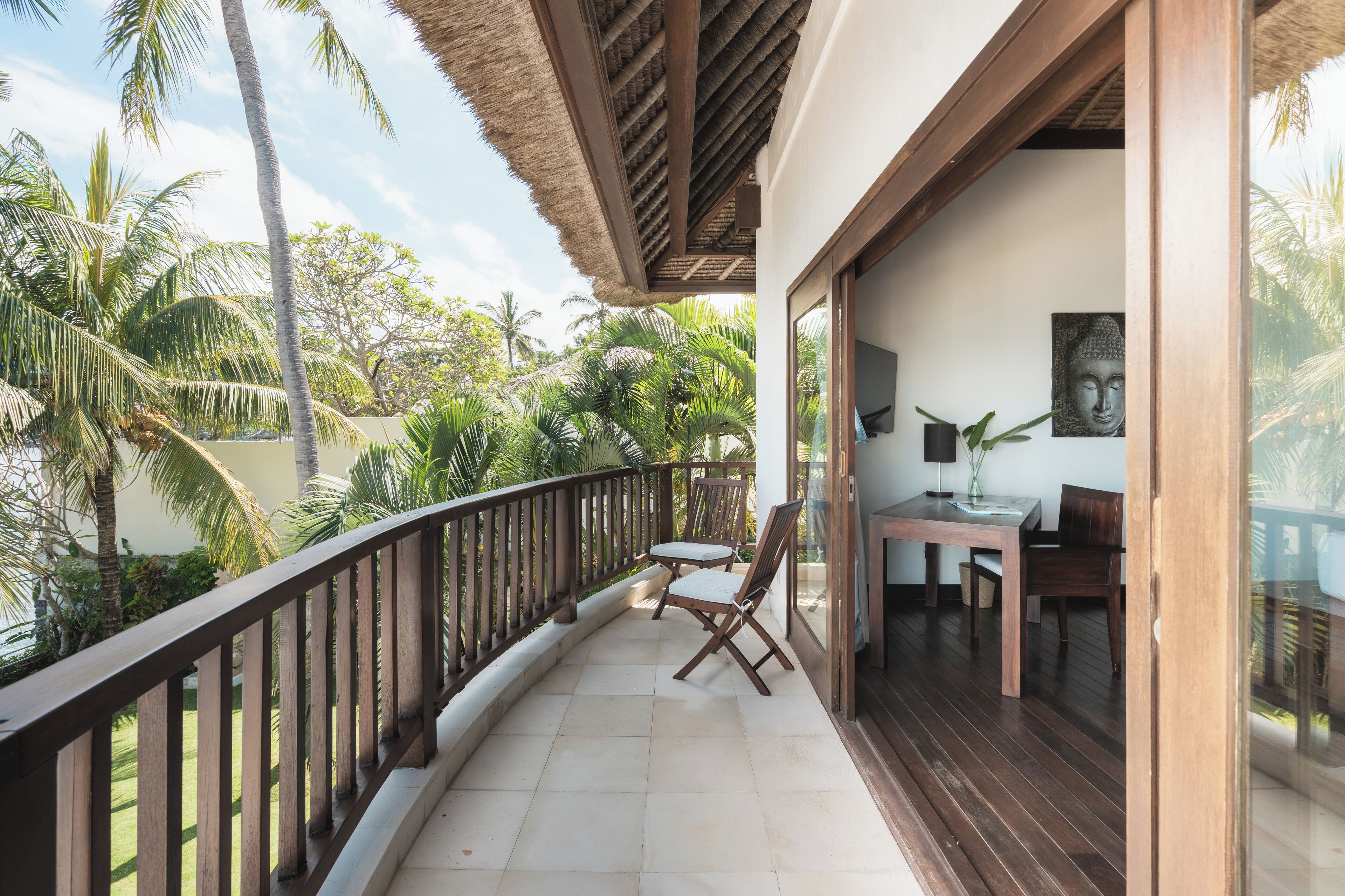 Un balcon avec une balustrade en bois, deux chaises en bois, une table et une statue de Bouddha.