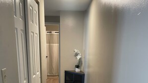 Un pasillo con alfombra gris, paredes blancas y un mueble de madera oscura con un jarrón blanco.