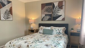 Un dormitorio con cama, dos mesitas de noche, una lámpara de pared, una planta en maceta y arte abstracto.
