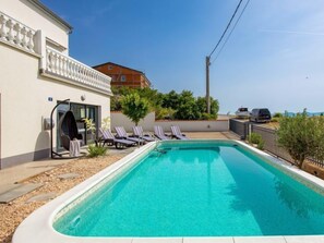 A swimming pool with lounge chairs, a covered seating area, and a view of a building in the background.