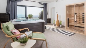 A modern hotel room with a large window, a hot tub, a seating area with chairs, and a wooden storage unit. - Villa Sunset view by Interhome (Senj)