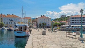 A harbor with a docked boat, stone-paved walkway, benches, and buildings with red-tiled roofs. - Villa Sunset view by Interhome (Senj)