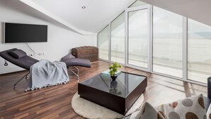 A modern living room with a sloped ceiling, a flat-screen TV mounted on the wall, a reclining chair, a small coffee table with a plant, and large floor-to-ceiling windows. - Villa Sunset view by Interhome (Senj)