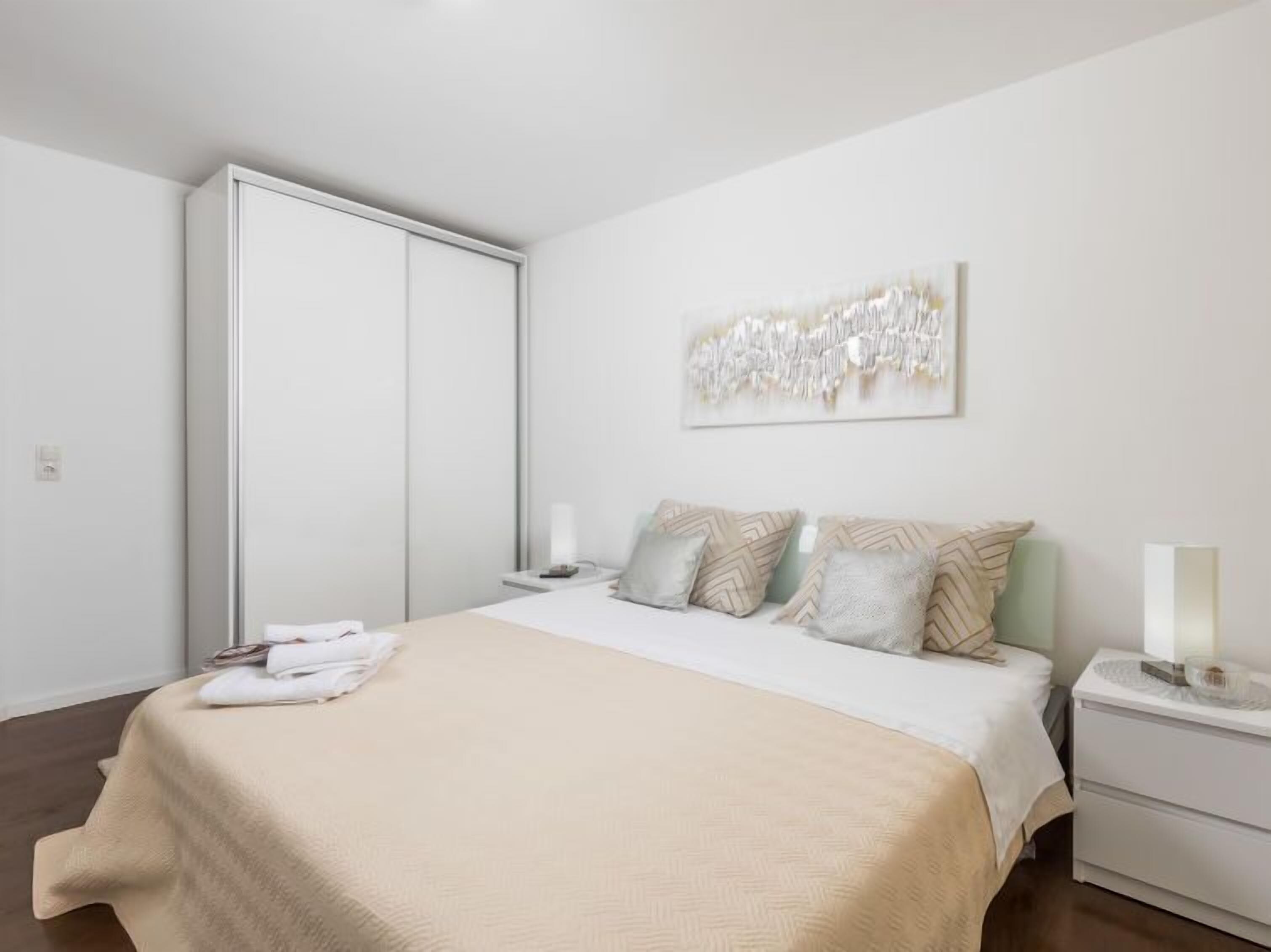 A bedroom with a bed, nightstands, a wardrobe, and a wall art piece.