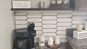 A kitchen with a coffee maker, a sign that says "Coffee bar love is brewing", and a hexagonal tile backsplash. - Cozy Farmhouse w/ short walk to a private  lake
 (Delton)
