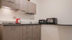 Une cuisine de taille réduite, avec des meubles de rangement en bois, un évier et deux micro-ondes noirs posés sur le plan de travail.