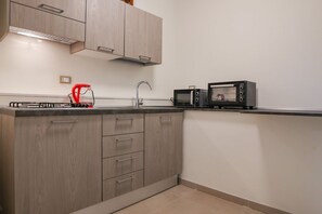 A compact kitchen with wooden cabinets, a sink, and two black microwaves on the countertop.