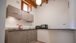 Une cuisine de taille réduite, avec des meubles en bois, une cuisinière à gaz, un four à micro-ondes et une fenêtre au-dessus de l’évier.