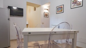 Un coin repas avec une table et des chaises blanches, un téléviseur à écran plat fixé au mur et des tableaux encadrés accrochés au mur.
