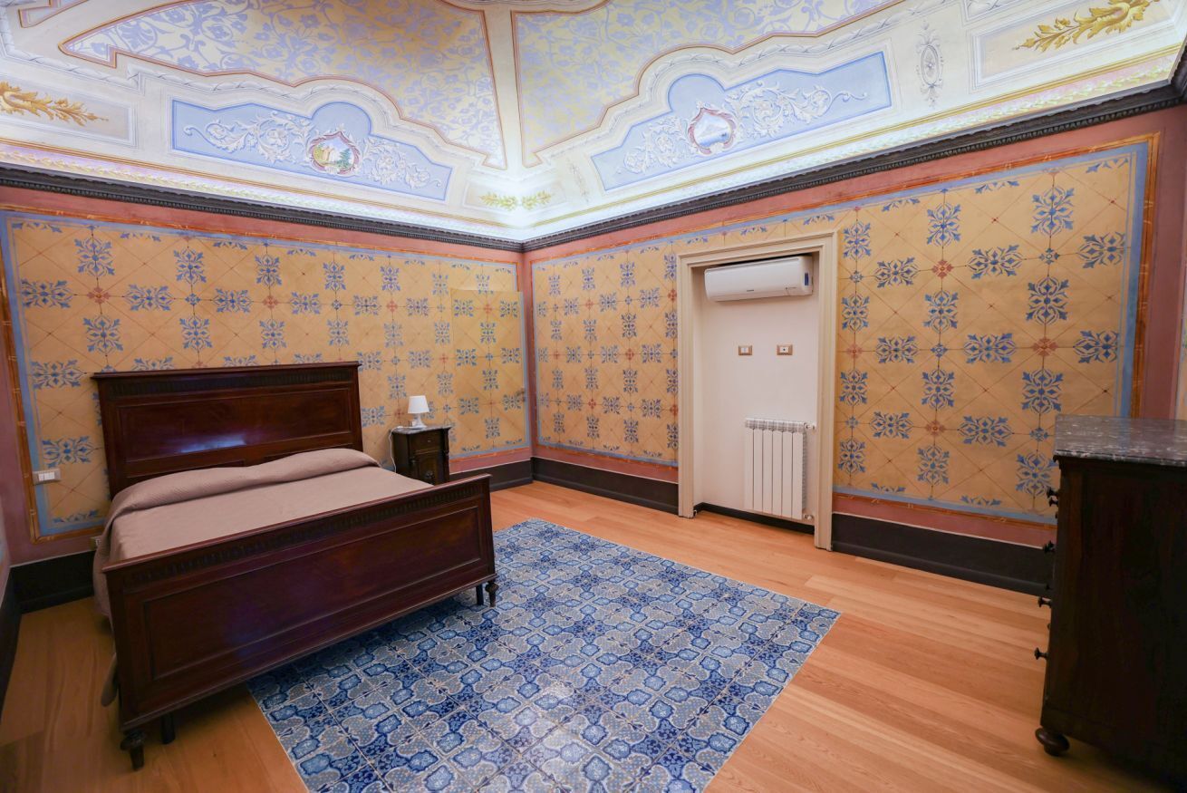 Ein Schlafzimmer mit einem hölzernen Bett, gemustertem Wandpapier und einem blauen Teppich.