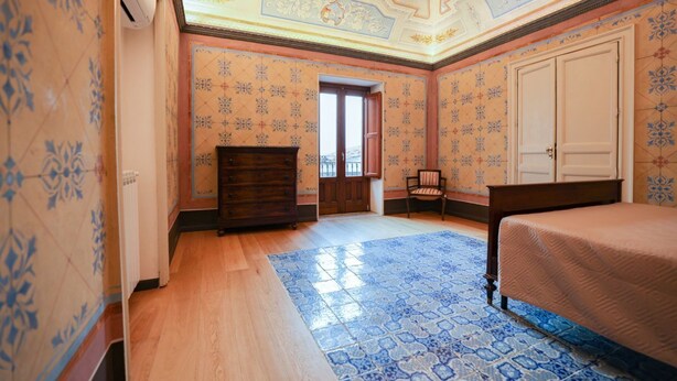 Une chambre à coucher avec un lit en bois, une commode, une chaise et un sol à motifs.