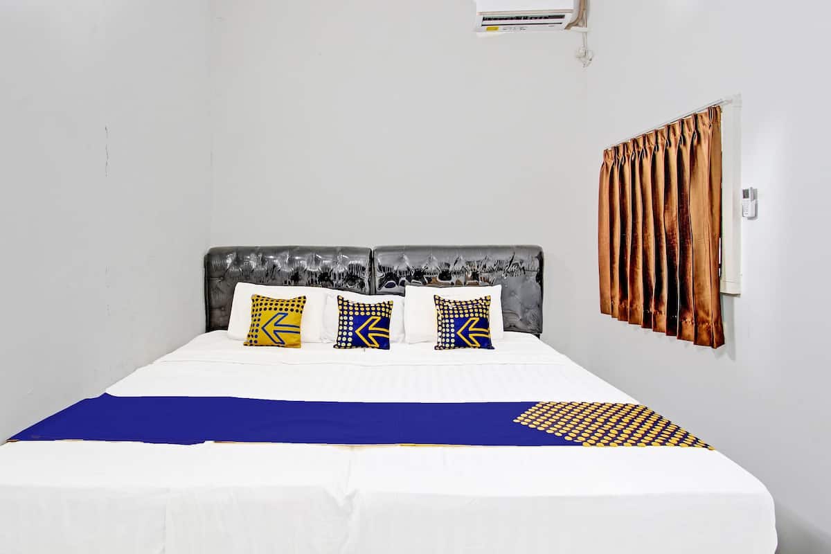 Un lit bien fait, recouvert d’une couvre-lit blanche et bleue, agrémenté de deux coussins à motifs et d’un plaid bleu.