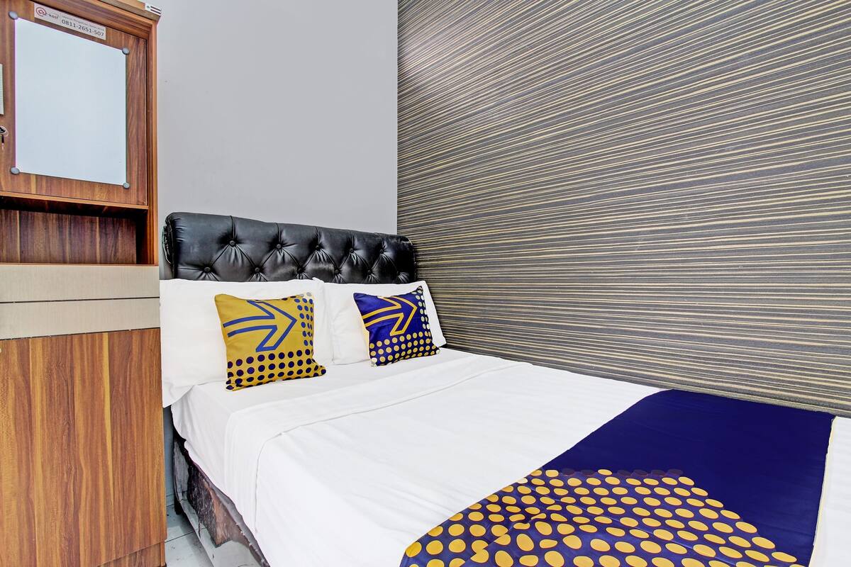 Une chambre d’hôtel avec une tête de lit en bois, un lit avec une literie blanche et un plaid aux motifs bleus et jaunes.