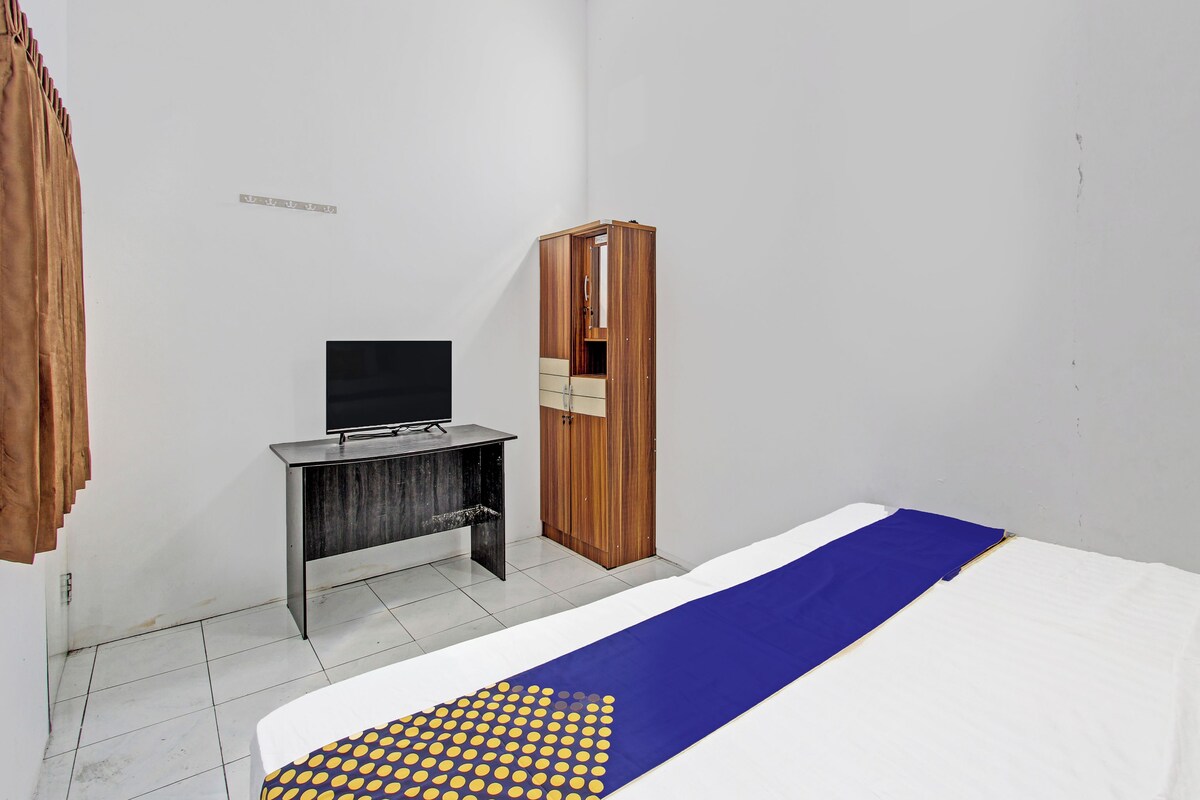 A hotel room with a bed, a desk with a flat-screen TV, a wardrobe, and a bathroom door.
