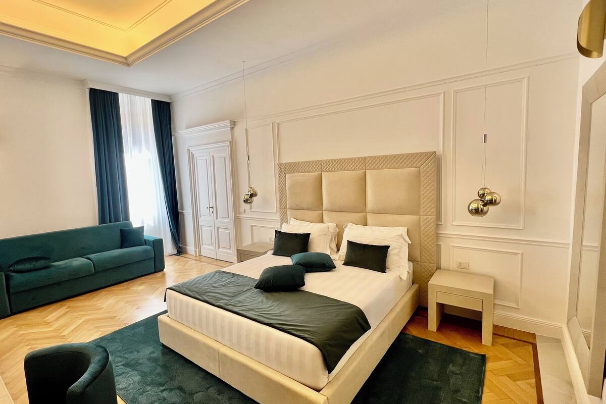 A hotel room with a large bed, a green sofa, a small table, and a wardrobe.