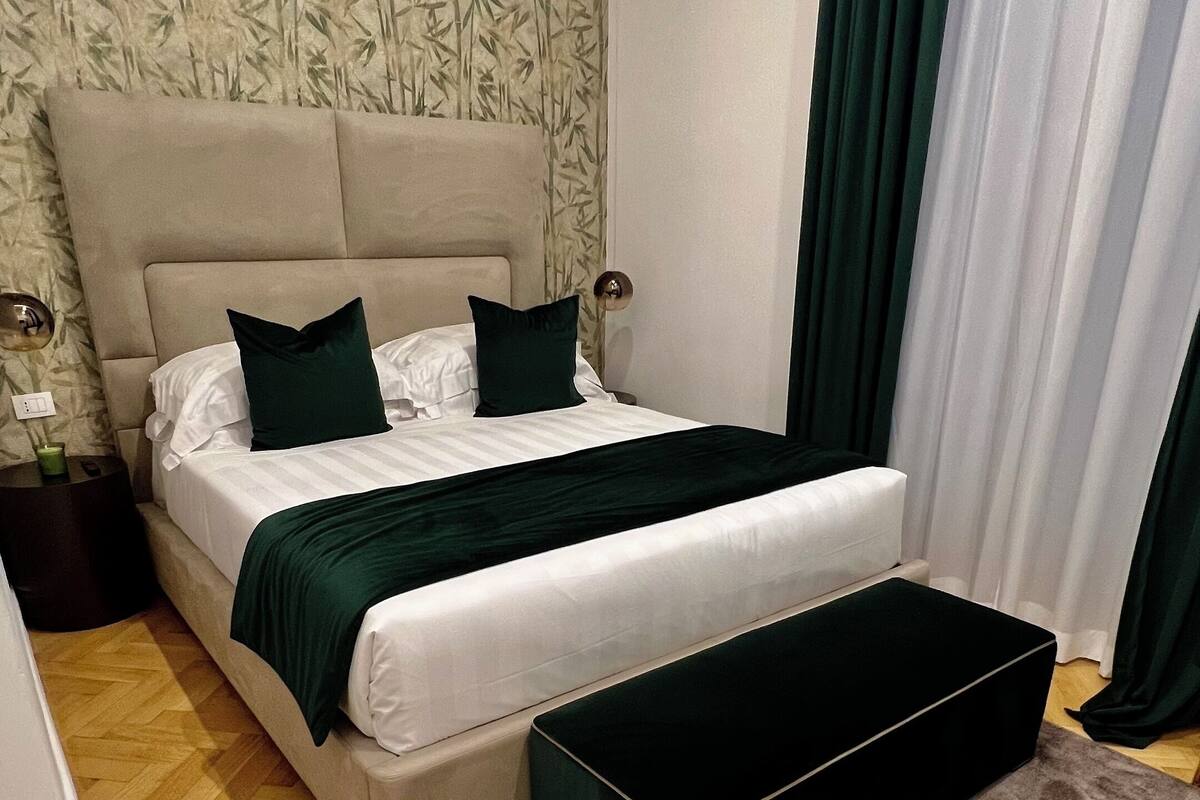 A modern bedroom with a large bed, a bedside table, a bench, and a patterned wallpaper.
