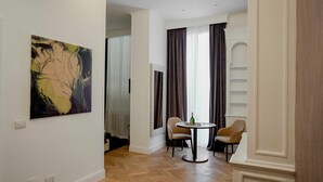 A modern living room with a large abstract painting, a dining area with two chairs and a table, and a view through a window with curtains. - Màs Boutique Hotel (Rome)