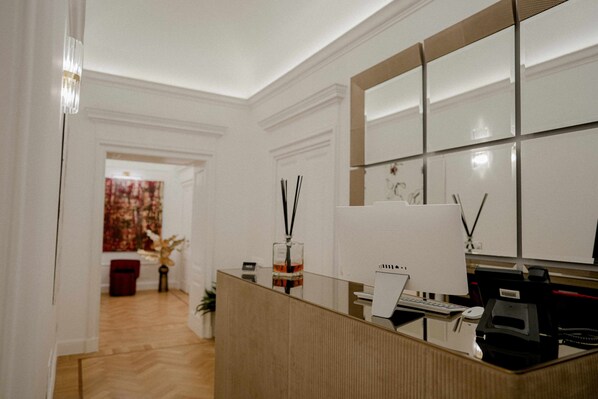 A reception area with a wooden reception desk, a large mirror, and a wall-mounted telephone. - Màs Boutique Hotel (Rome)